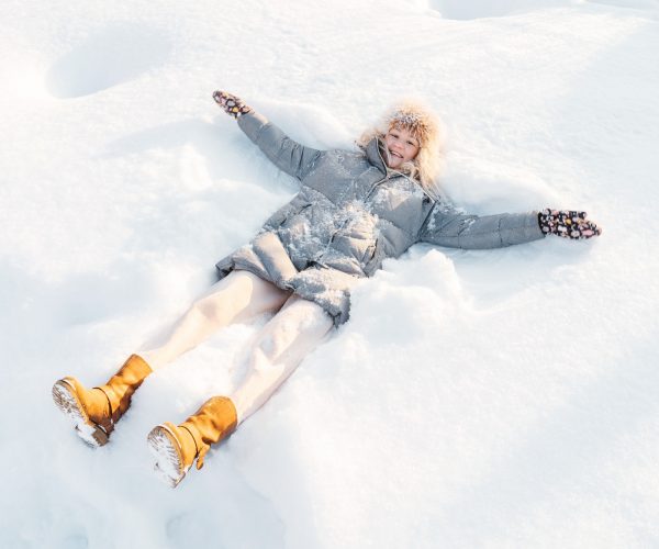 Woman lying in snow making snow angel.